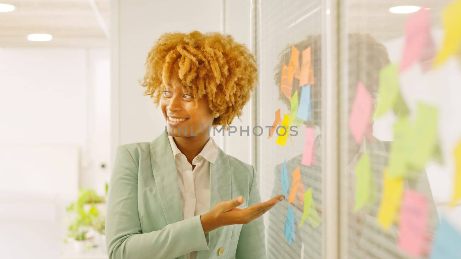 Woman pointing a post-it presenting ideas in a meeting by ivanmoreno