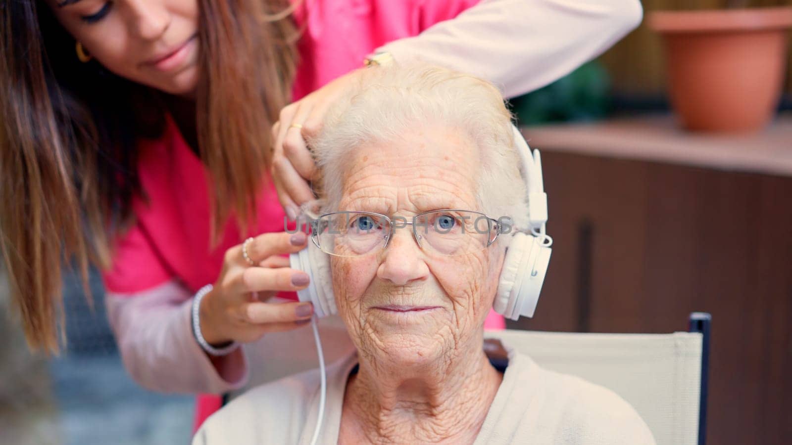 Nurse adjusting headphones to a senior woman in a geriatric by ivanmoreno