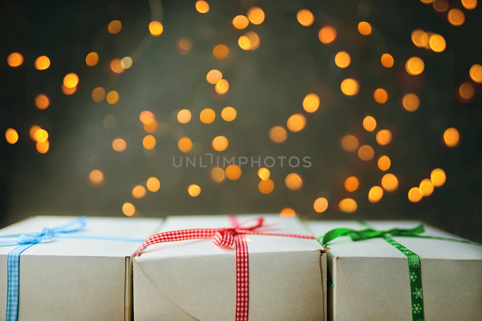 Stack of gift wrapped Christmas presents. The pile of gifts is stacked neatly on the table with a garland in the background. Side view.