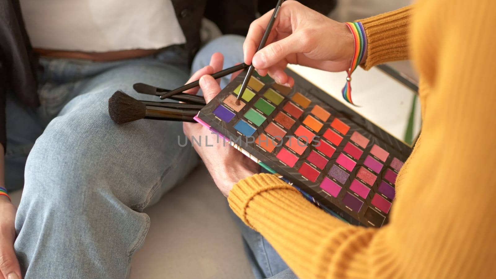 A person picking up powder from the colour palette of a make-up kit.