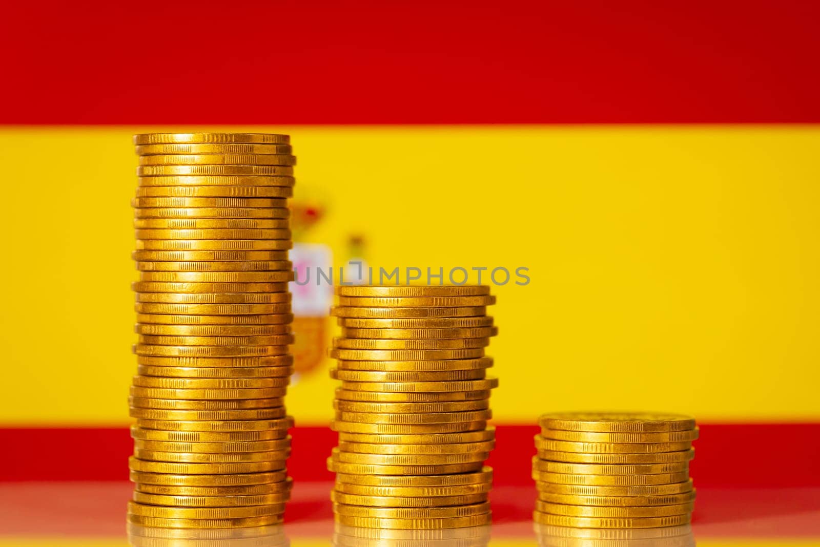 Three golden coin stacks from highest to lowest against flag of Spain by VitaliiPetrushenko
