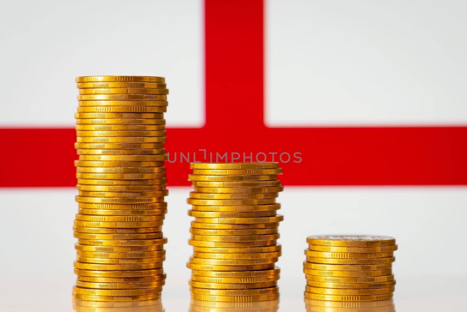 Three golden coin stacks from highest to lowest against flag of England by VitaliiPetrushenko
