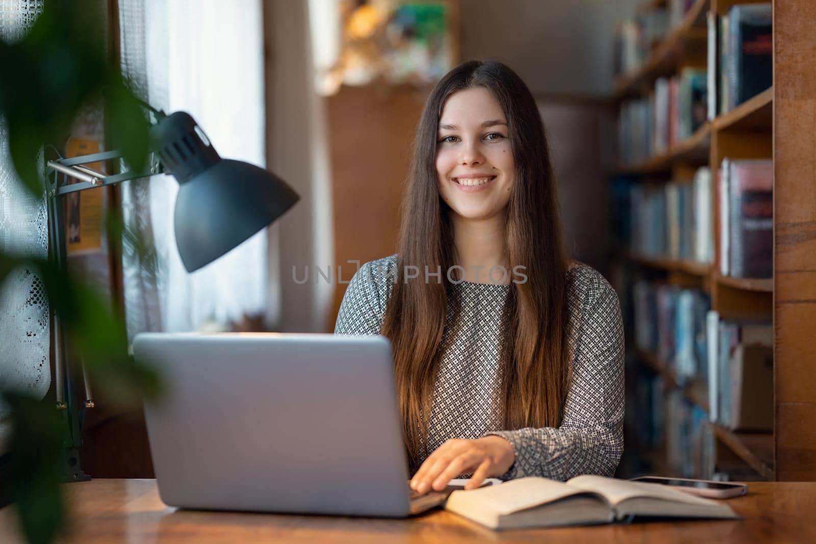 Portrait of a smiling girl college student doing assignment in library