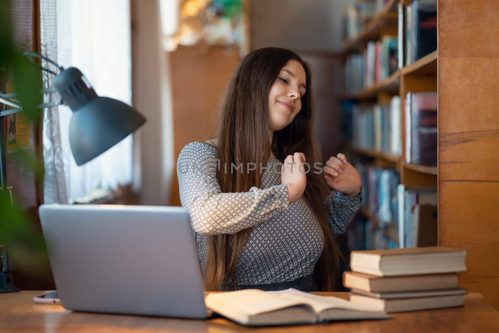 University student having physical excercises after long hours of work, working in library by VitaliiPetrushenko