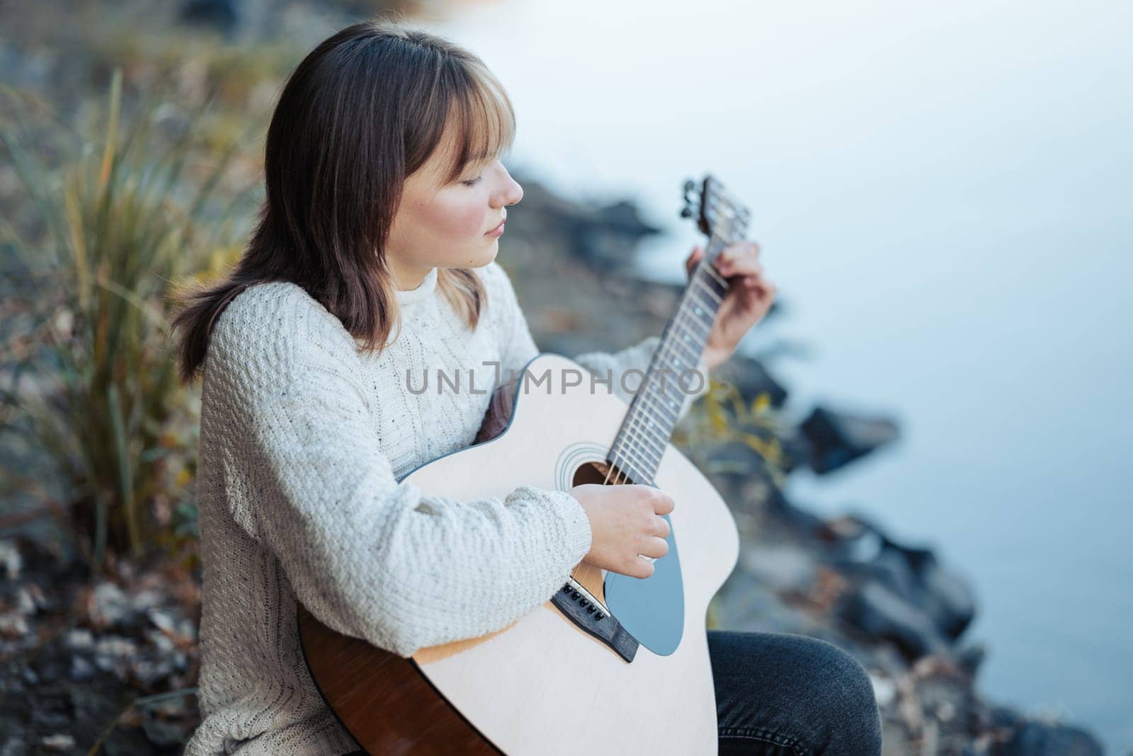 Girl practicing playing the guitar, looking on the water