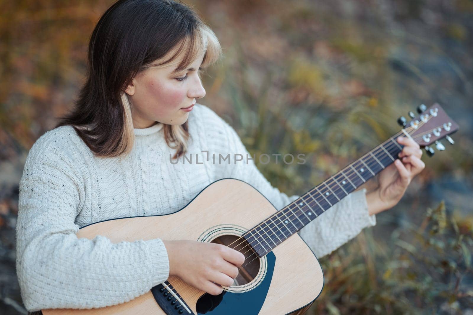 Portrait of a young girl playing the guitar outdoors, mastering her skills