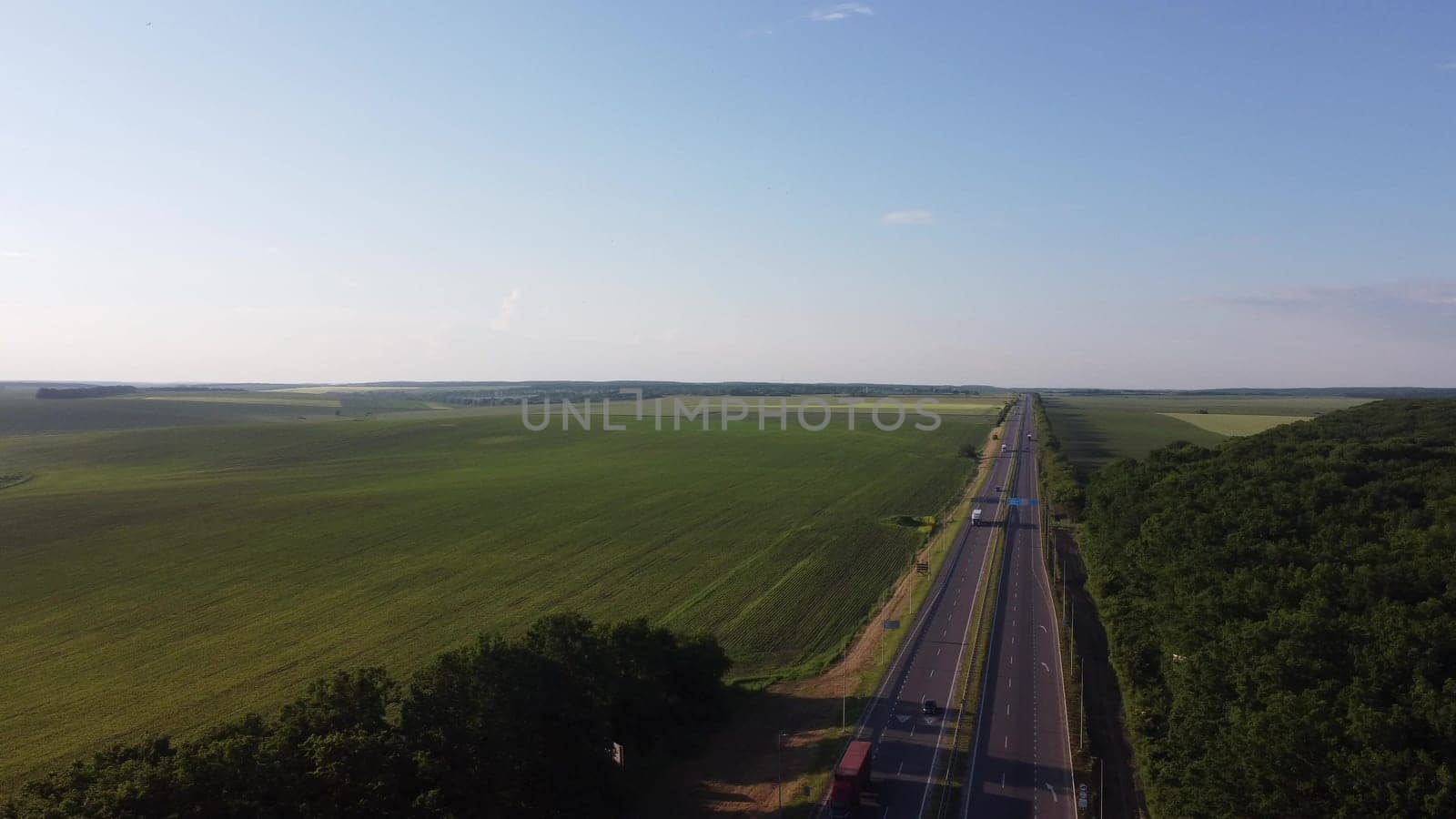 Aerial view on highway road through green fields on a summer sunny day. 4k footage of landscape with asphalt freeway between meadow and rural field. Drone shoots video of the countryside
