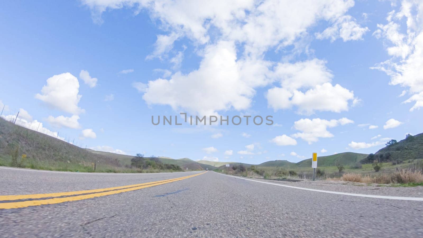 On a clear winter day, a car smoothly travels along Highway 101 near Santa Maria, California, under a brilliant blue sky, surrounded by a blend of greenery and golden hues.