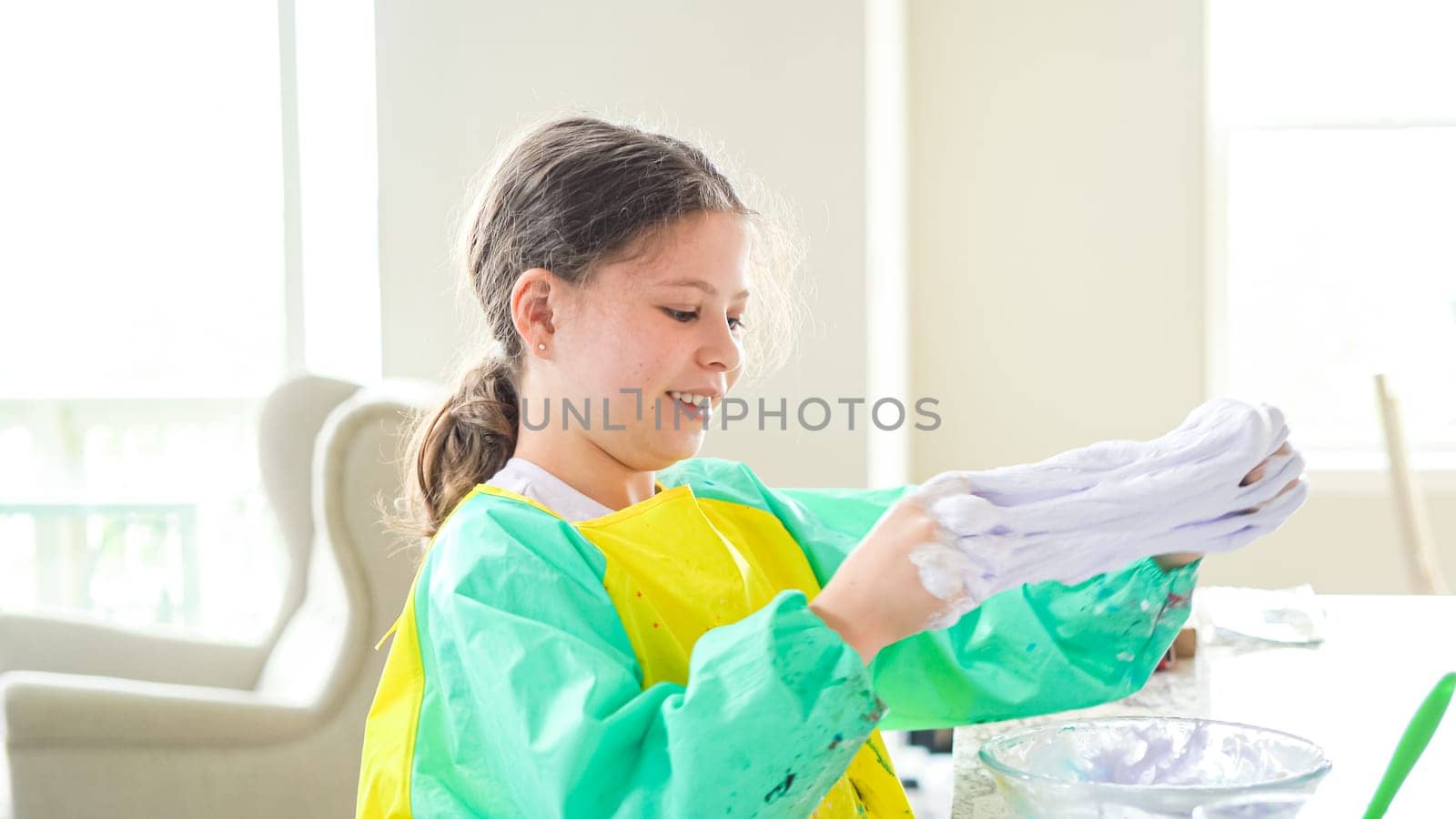 In a modern kitchen, a homeschooled girl is engrossed in creating homemade slime, a fun and educational hands-on project that enhances her creativity and problem-solving skills.