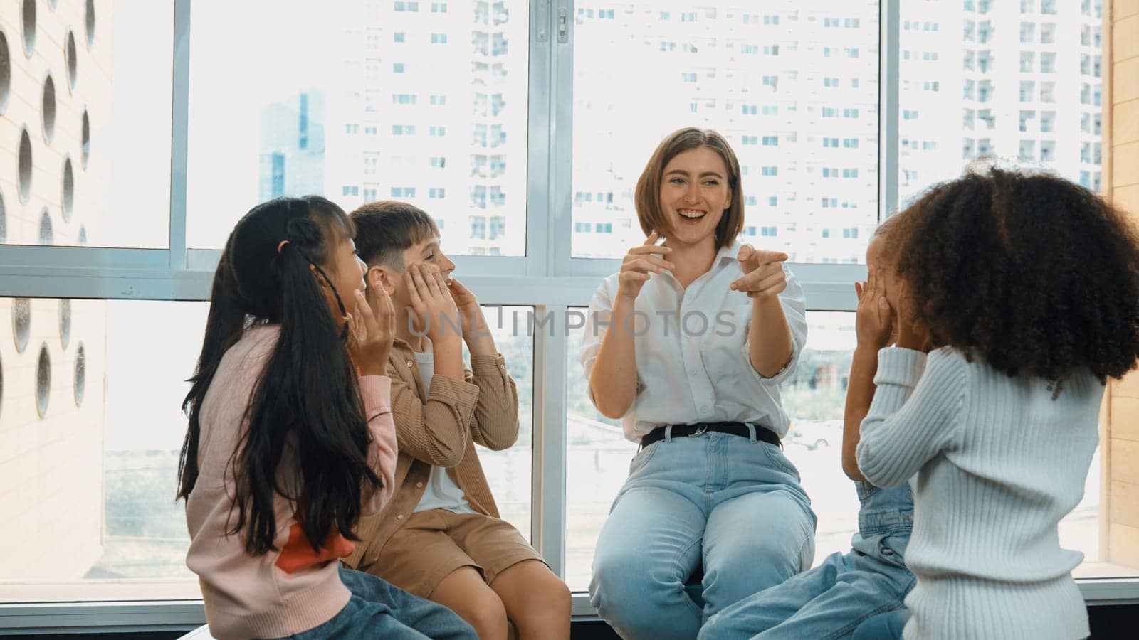 Smart caucasian teacher teaching while sitting on floor together surrounded by diverse students. Professional instructor playing with multicultural learner. Creative education concept. Erudition.