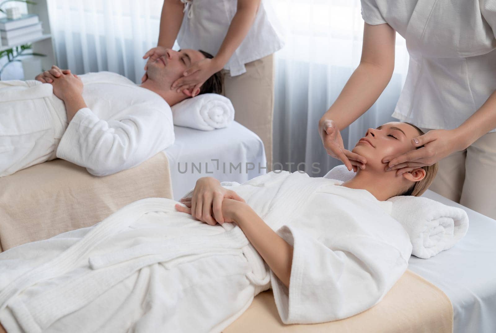 Caucasian couple enjoying relaxing anti-stress head massage and pampering facial beauty skin recreation leisure in dayspa modern light ambient at luxury resort or hotel spa salon. Quiescent