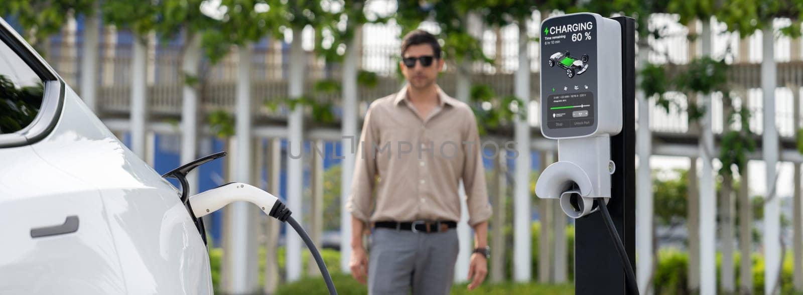 Young man recharge electric car's battery from charging station. Expedient by biancoblue