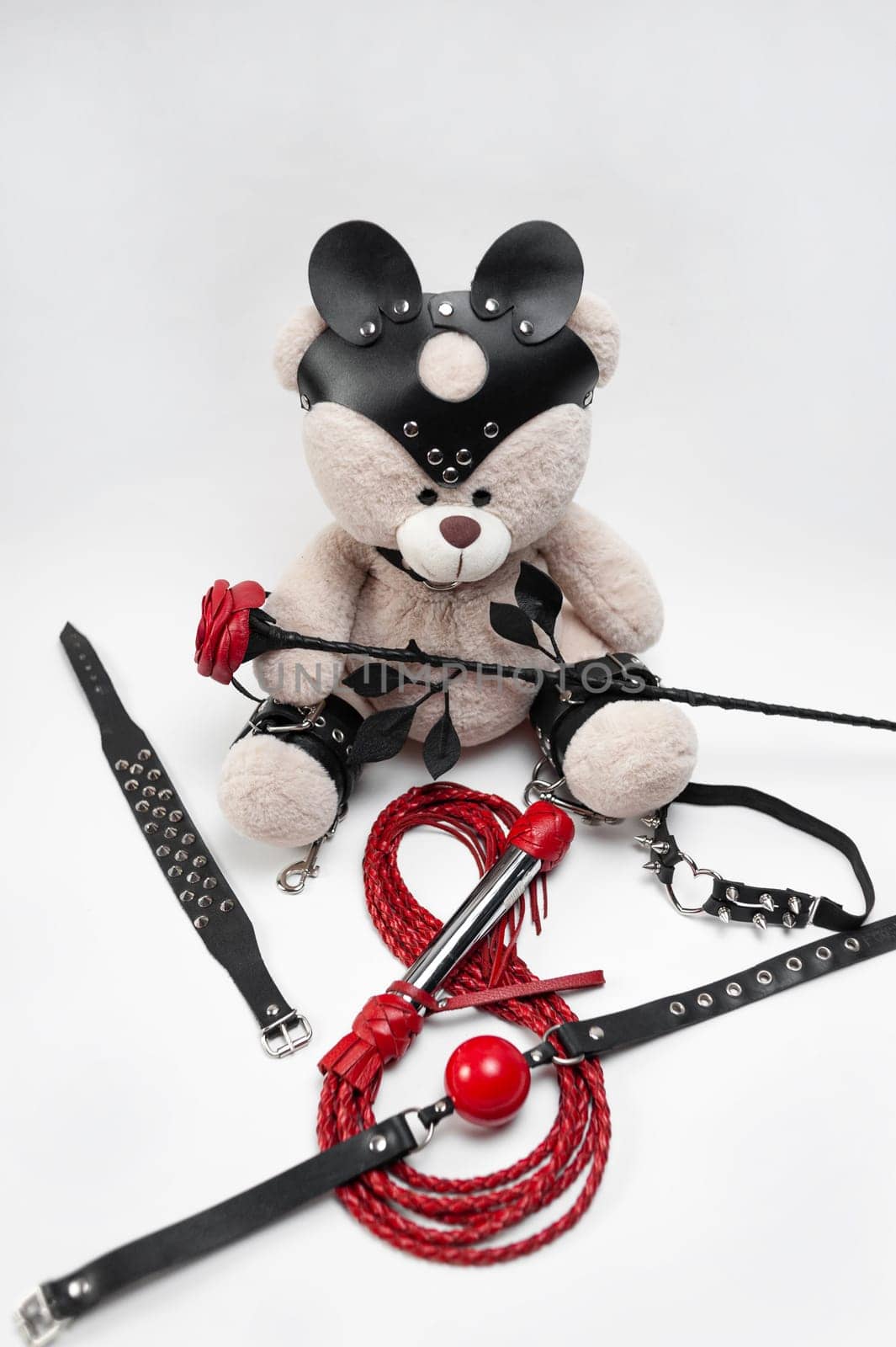 For the celebration of March 8, women's Day, a set of sexy accessories for bdsm games from a sex shop on a white background with a cute teddy bear by Rotozey