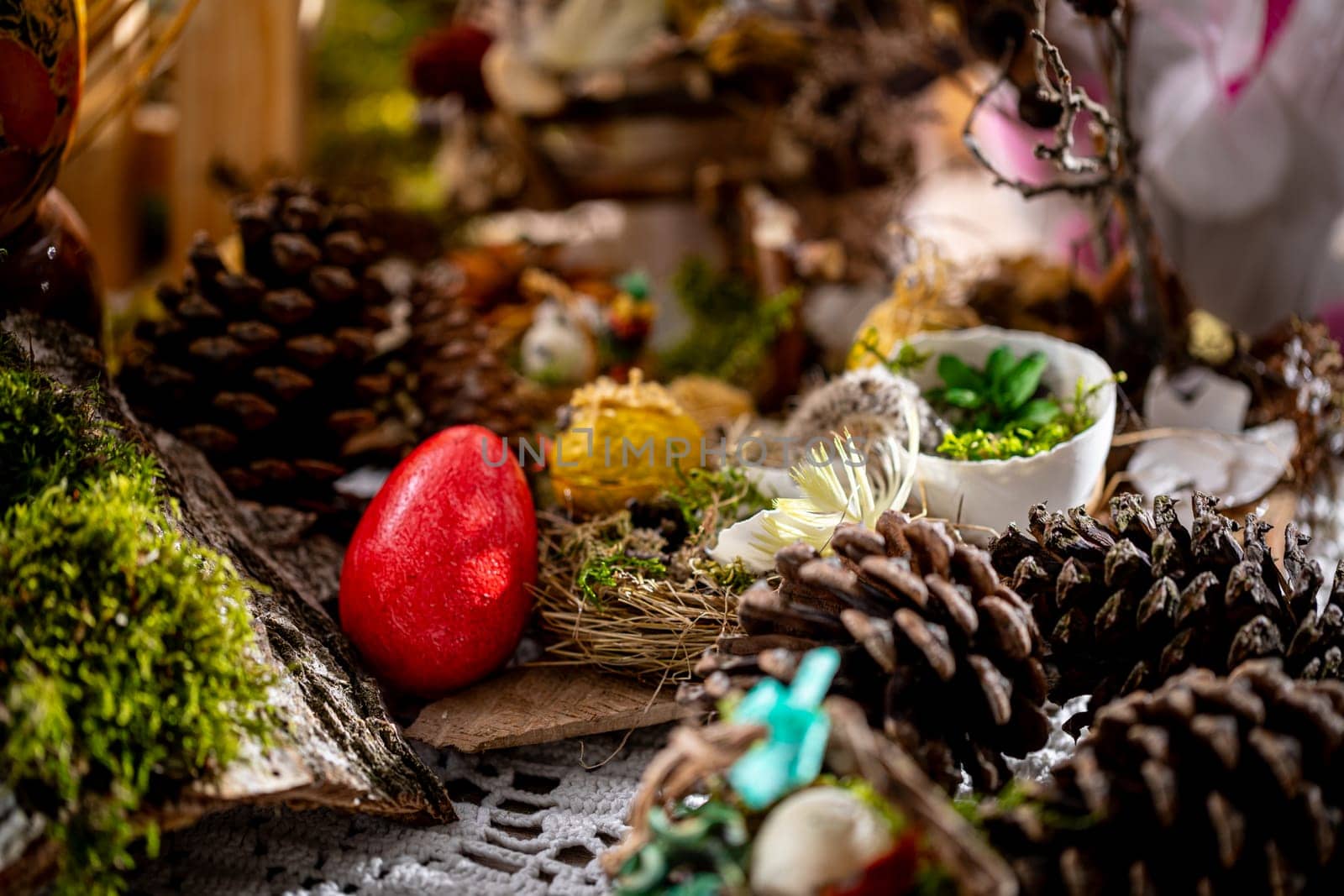 In this captivating Easter scene, a single handcrafted red egg rests among a variety of rustic decorations, including pine cones, bird nests, green moss, birch bark, and bird feathers.