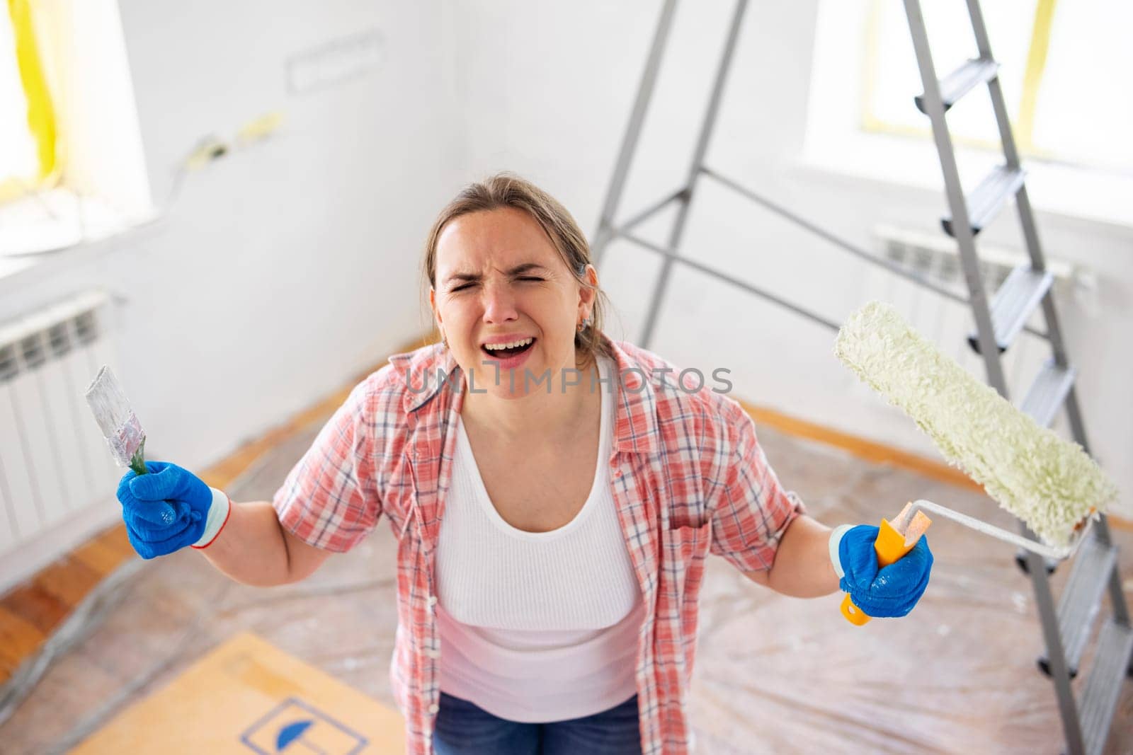 Frustrated woman with paintbrush and roller during home renovation.
