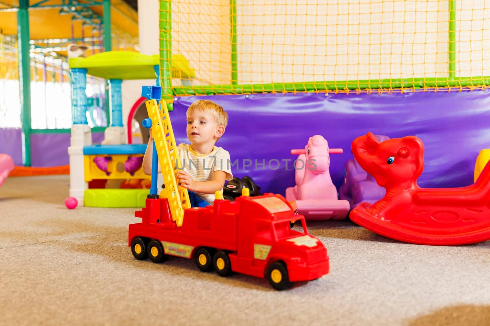 A young boy attentively plays with a colorful toy crane in a vibrant indoor playroom setting.