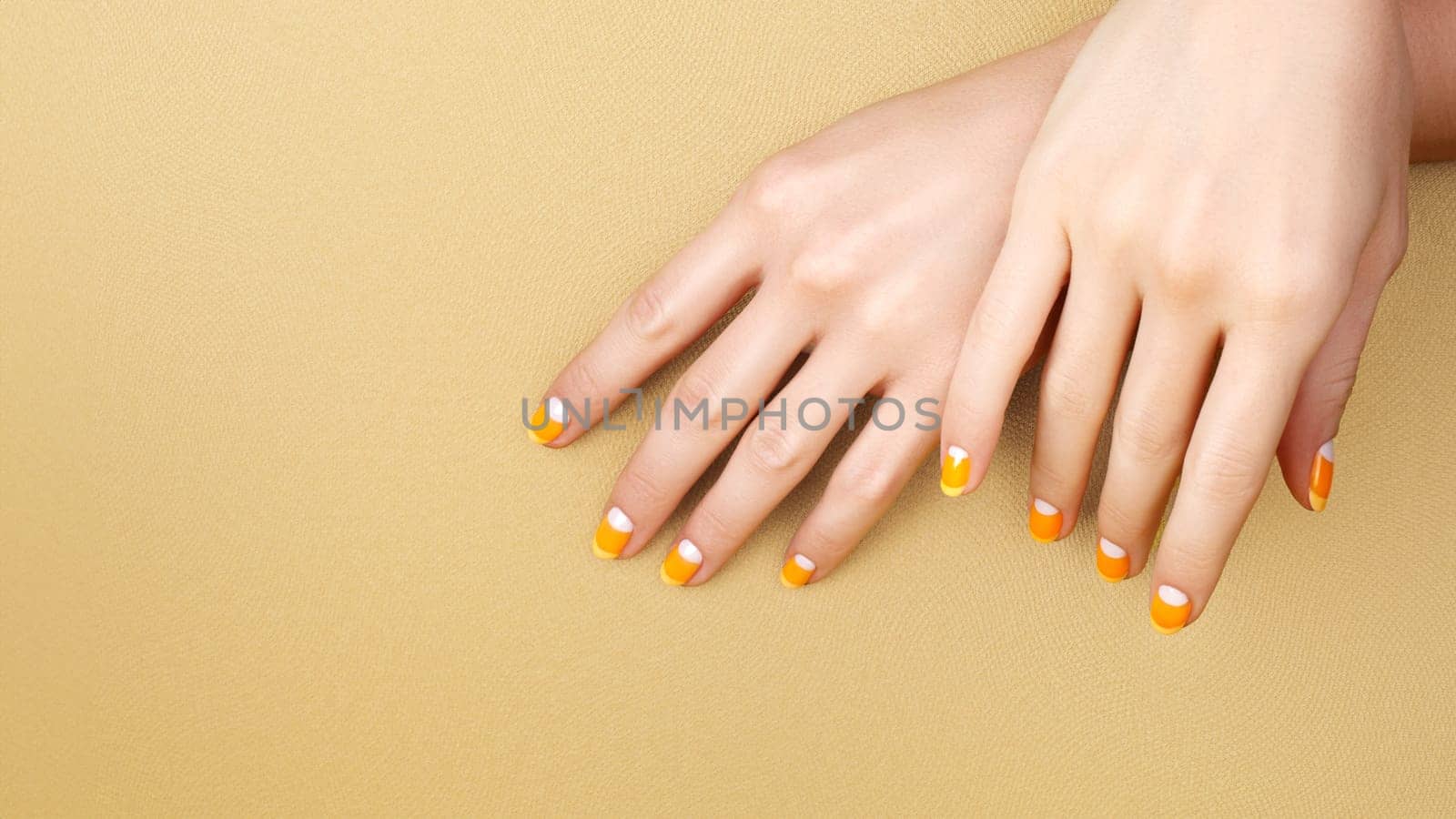 Beautiful Female Hands with bright Orange Manicure like Candy Corn on Yellow Background. Manicured Nails with Creative Gel Polish Design. Halloween Style