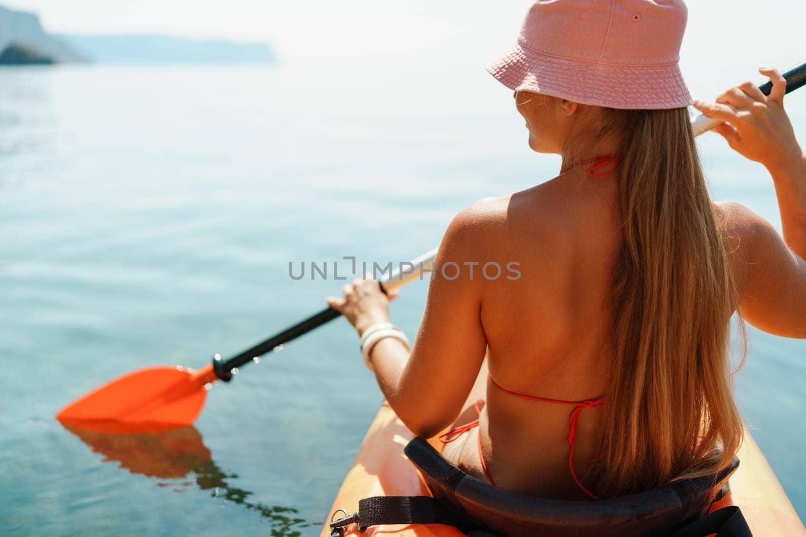 Woman in kayak back view. Happy woman with long hair in a swimsuit and hat floating in kayak on the sea. Summer holiday vacation. Summer holidays vacation at sea