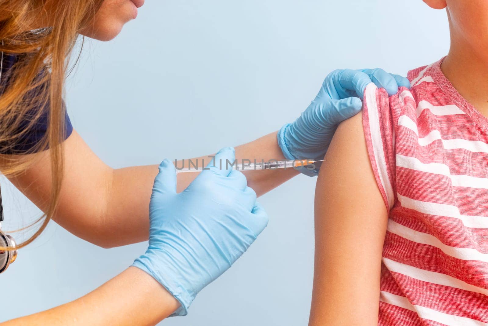 A healthcare professional administering a vaccine to a child's arm with a syringe, both wearing casual clothing.