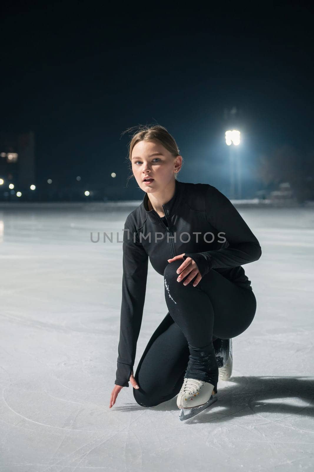 Beautiful young woman ice skating and performing short program over city outdoor ice arena. Winter activities concept