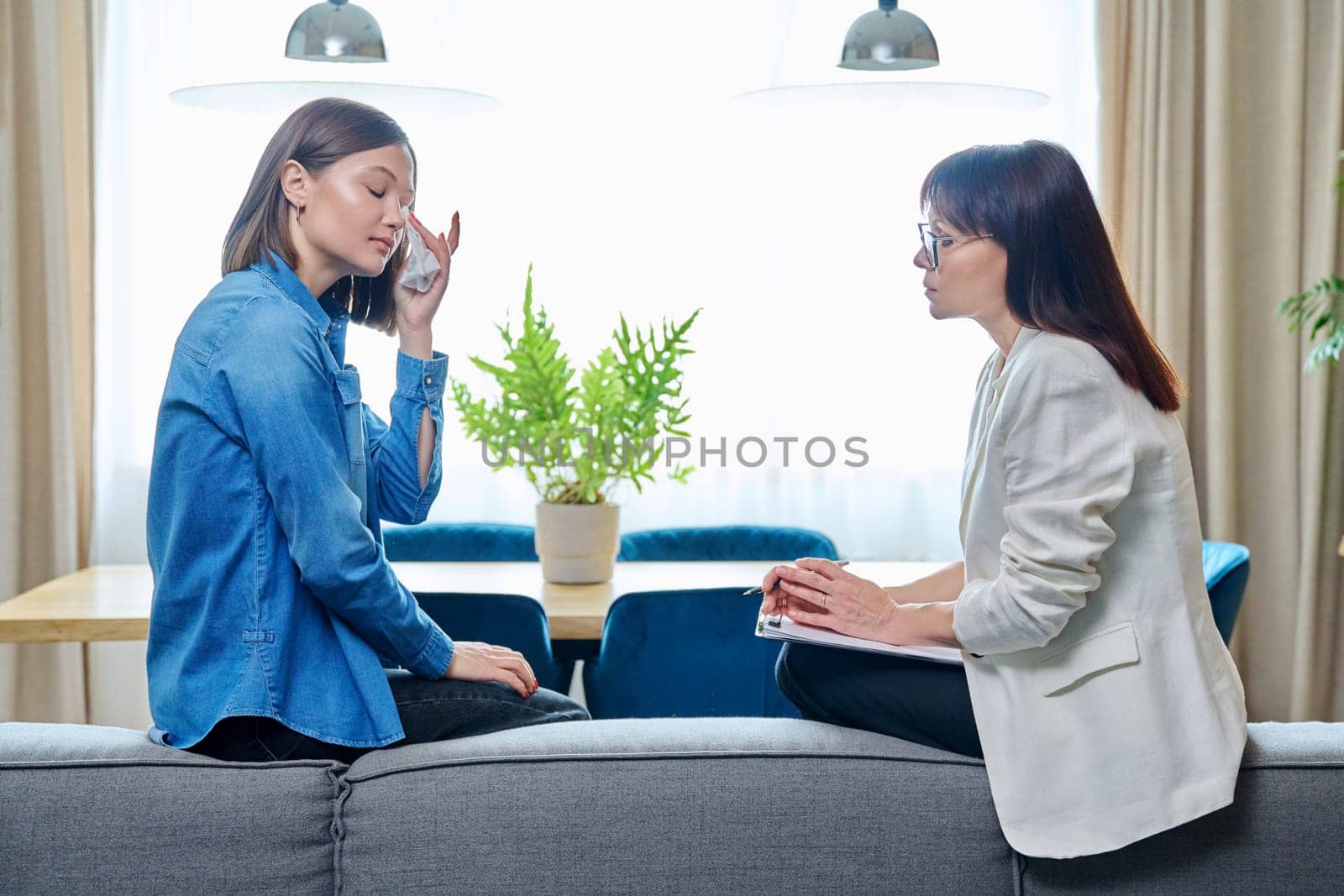 Sad young woman in meeting with psychologist, sitting on couch in office by VH-studio