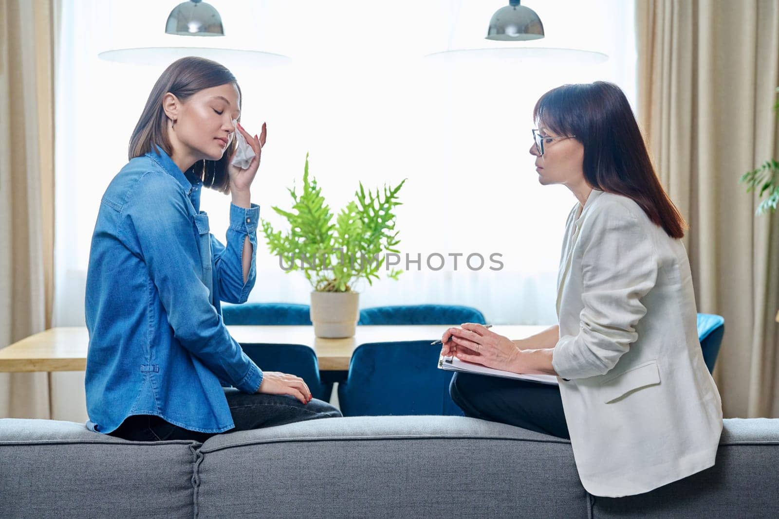 Sad crying young 20s woman in meeting with female psychologist therapist counselor sitting on couch in office. Psychology, therapy, psychotherapy, treatment, mental health, help, support