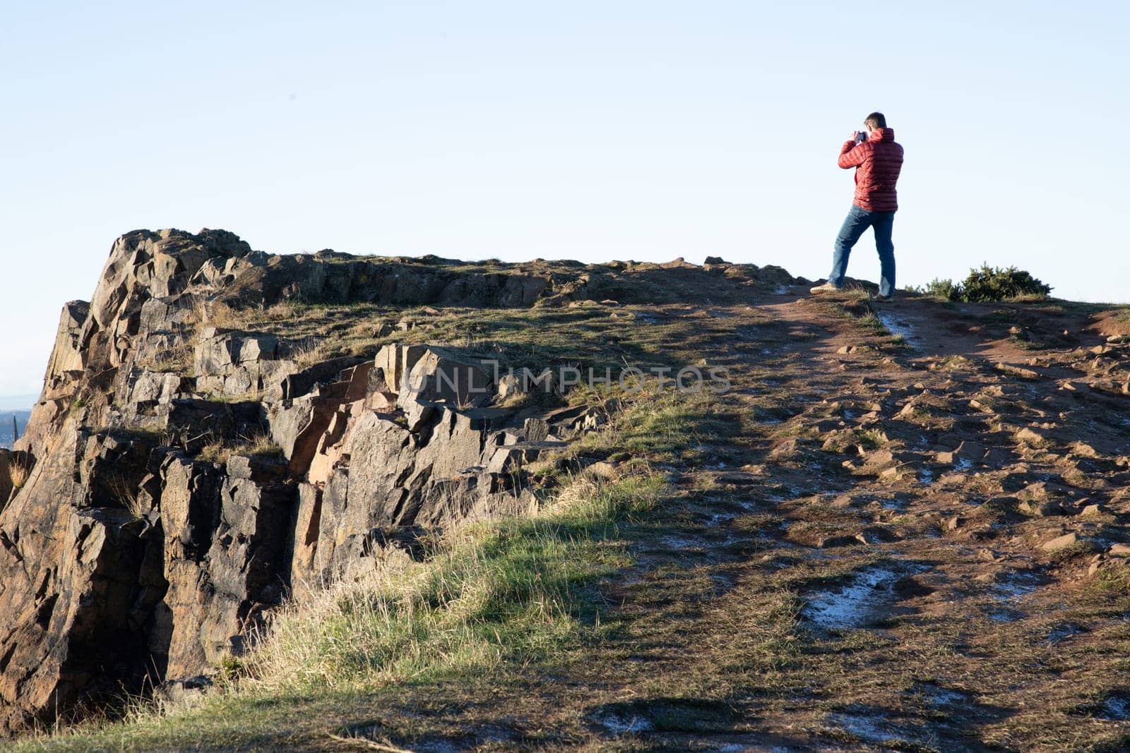 Edinburgh, Scotland - Jan 17, 2024 - A beautiful view of a person over a top of a high mountain on Salisbury Crags looking to a cityscape. Destinations in Europe, Space for text, Selective focus.
