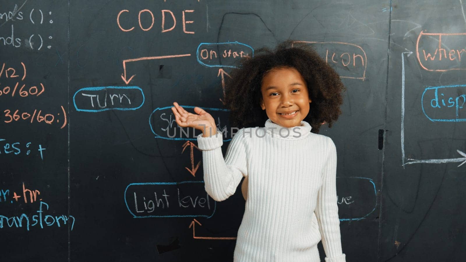 Happy african girl writing blackboard and turnaround to waving at camera while standing at board with engineering prompt or coding, programing system written in STEM technology classroom. Erudition.