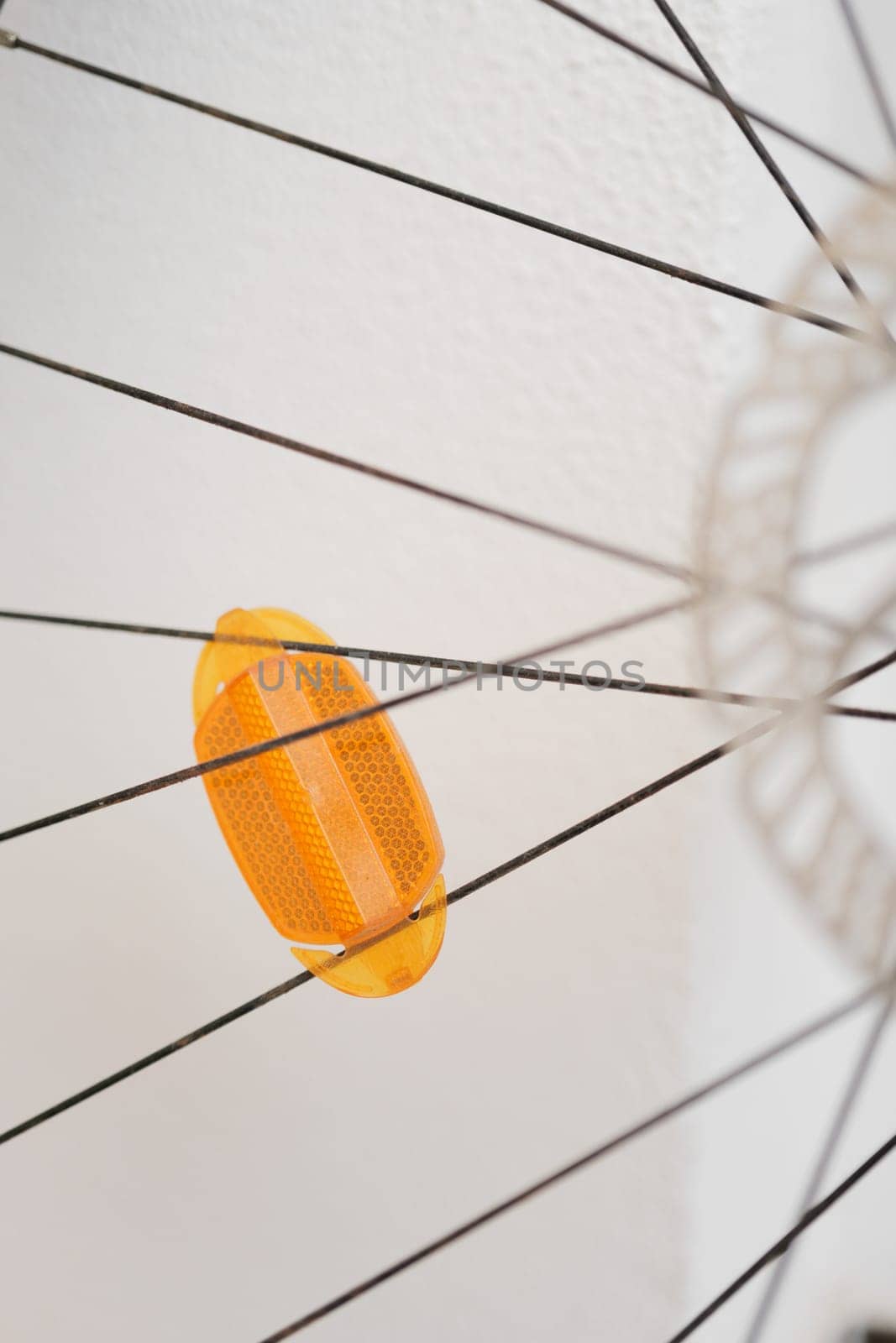 Abstract View of a Yellow Bicycle Reflector Between Spokes Against a White Wall by apavlin
