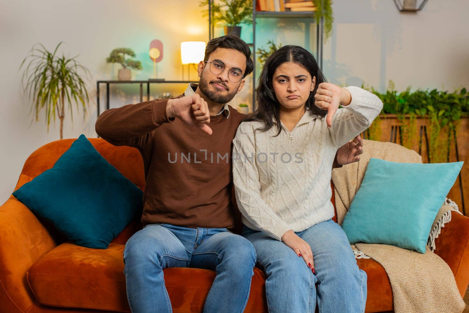 Upset Indian couple showing thumbs down gesture, expressing discontent, disapproval, dissatisfied by efuror