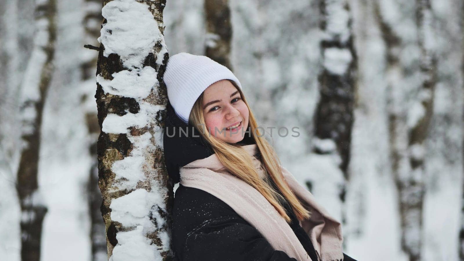 A girl is walking through the woods and kicking up snow in a birch forest