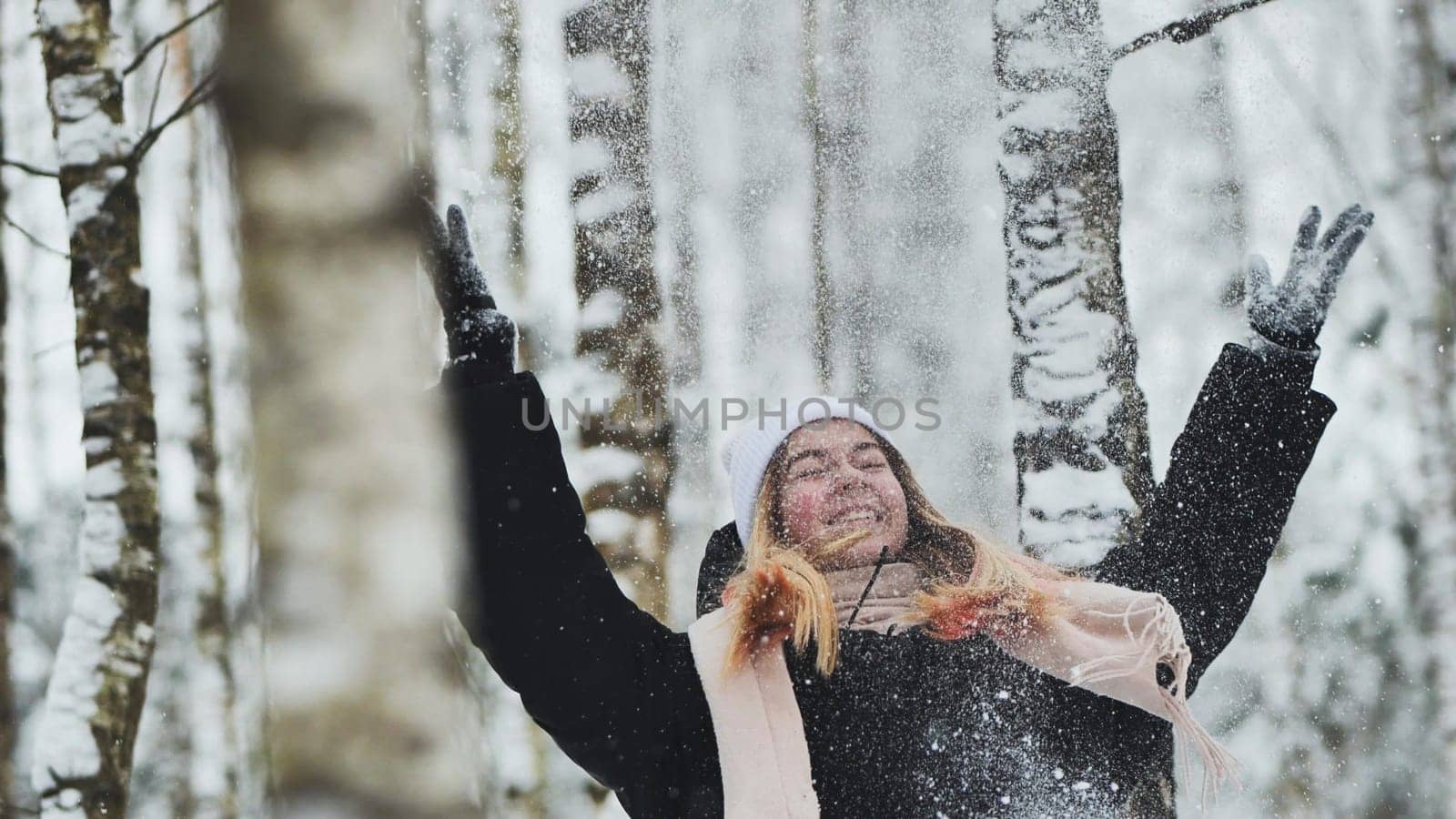 A girl is walking through the woods and kicking up snow in a birch forest