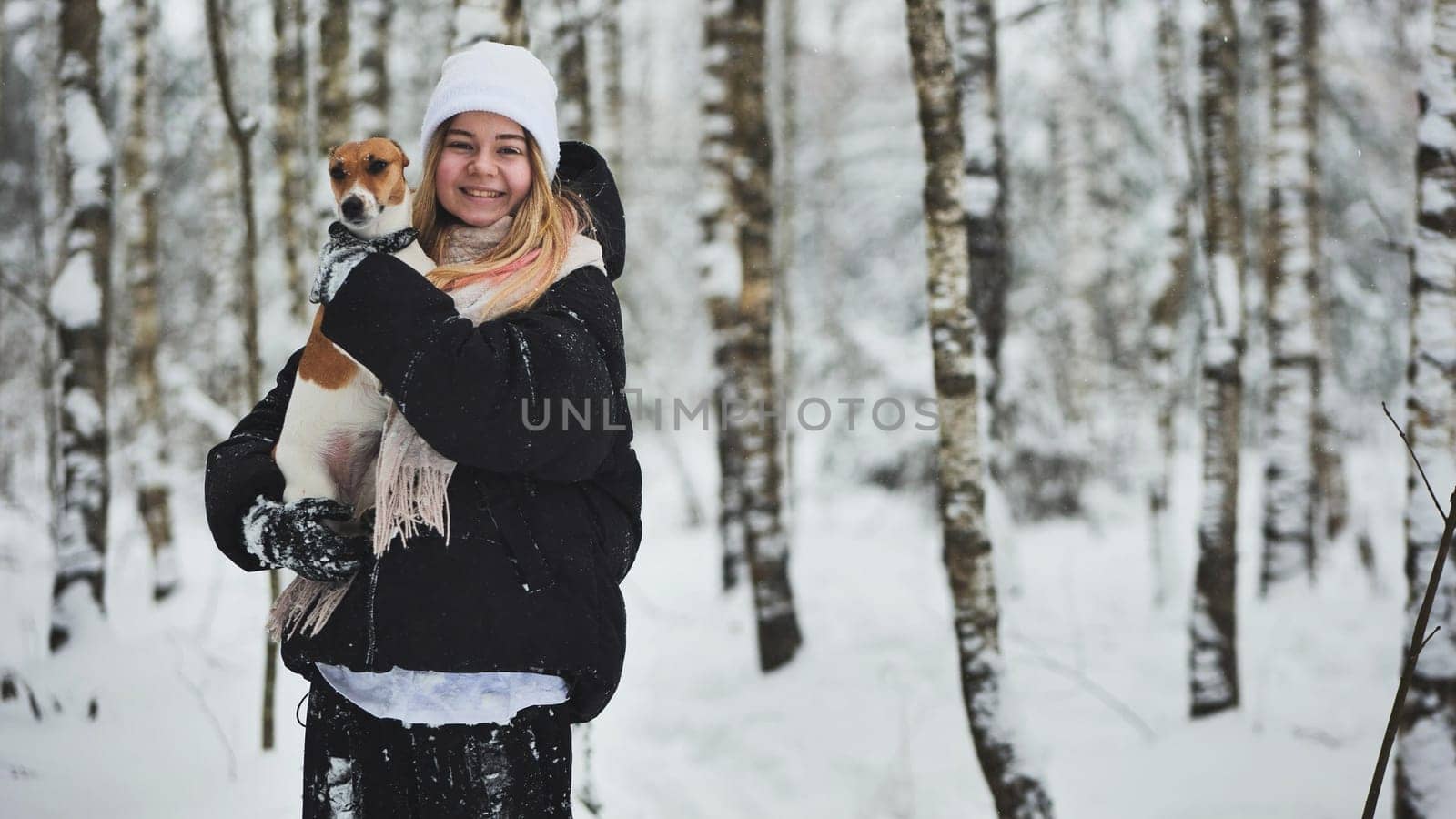 A girl kisses a Jack terrier dog in the winter woods