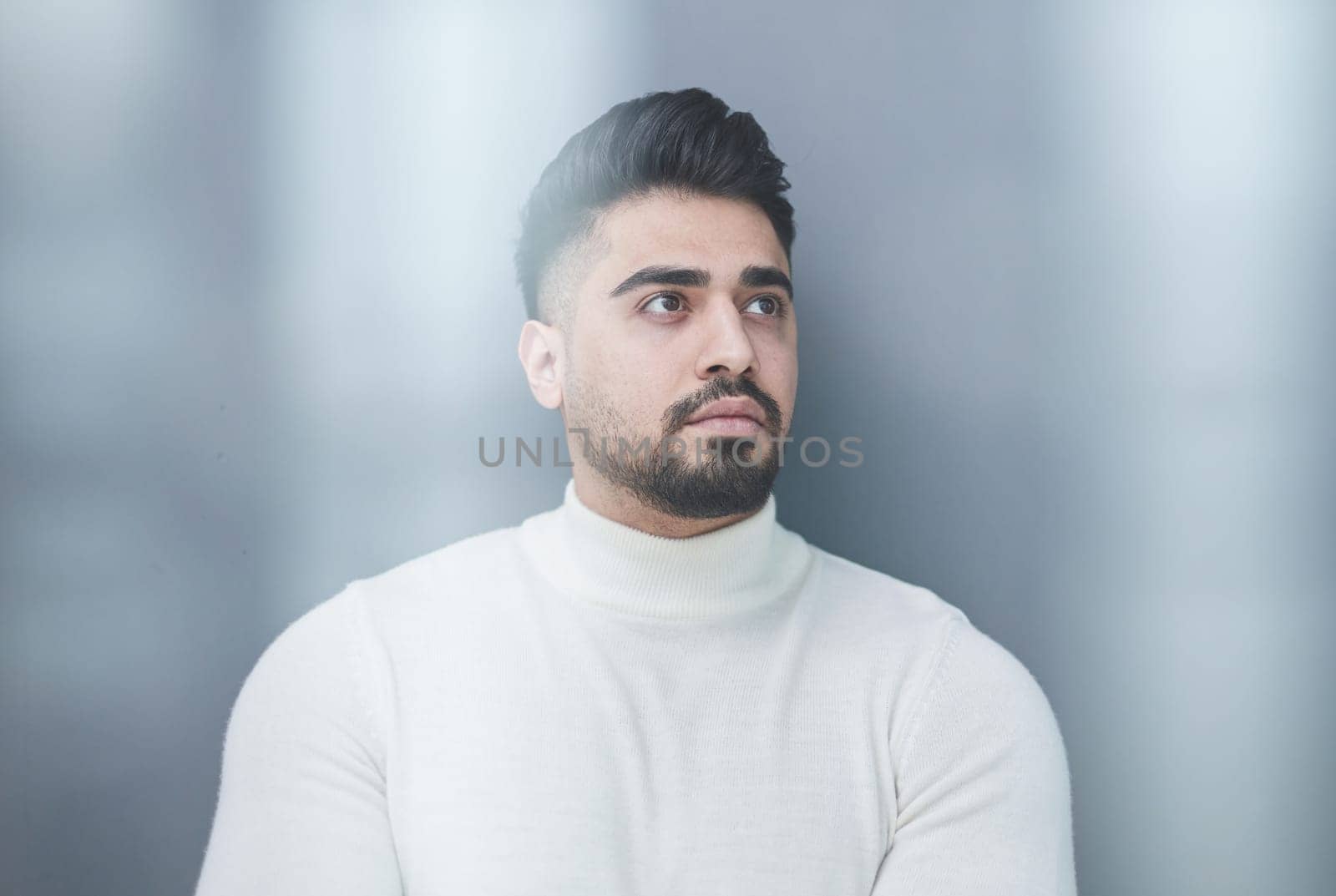 Portrait of a stylish man posing on a gray background with his arms crossed