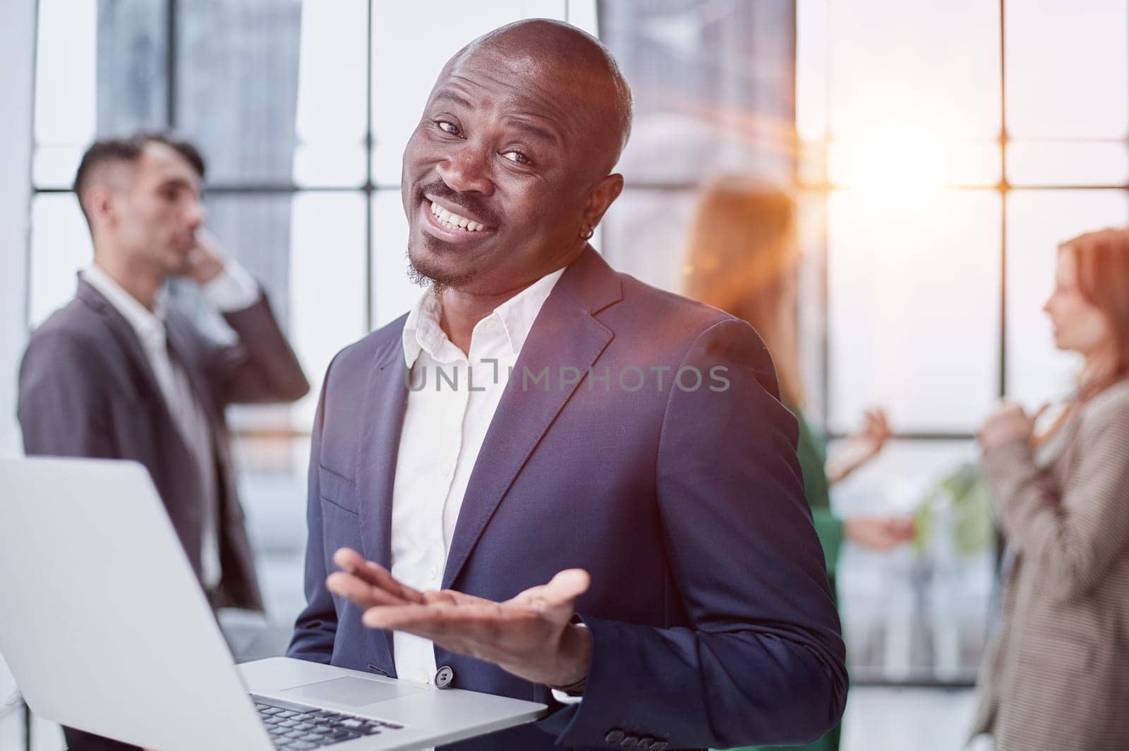 Young African American man in a business suit holding a laptop against the background of his colleagues