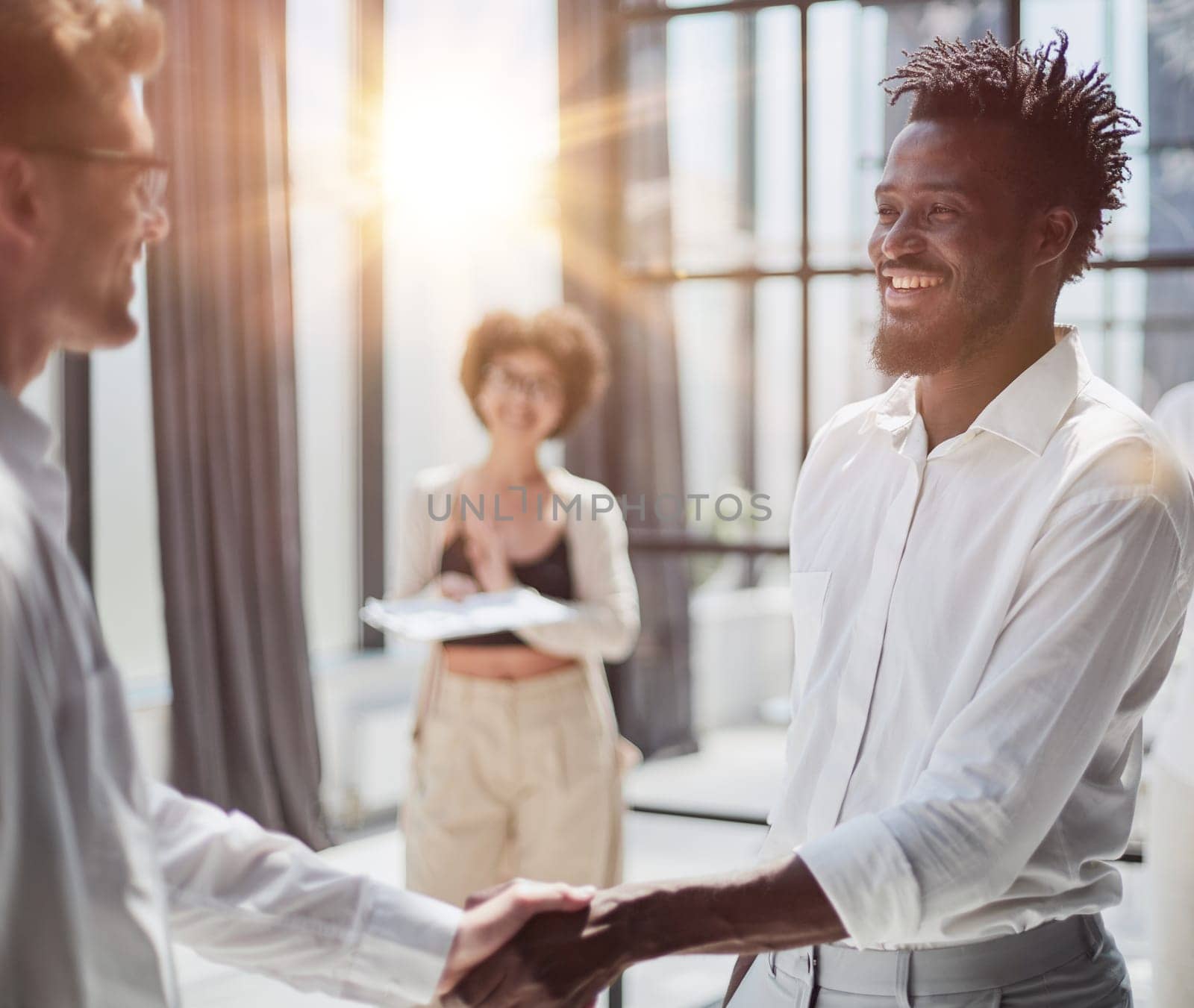 Glad to work with you. Young modern men in smart casual wear shaking hands and smiling while working in the creative office