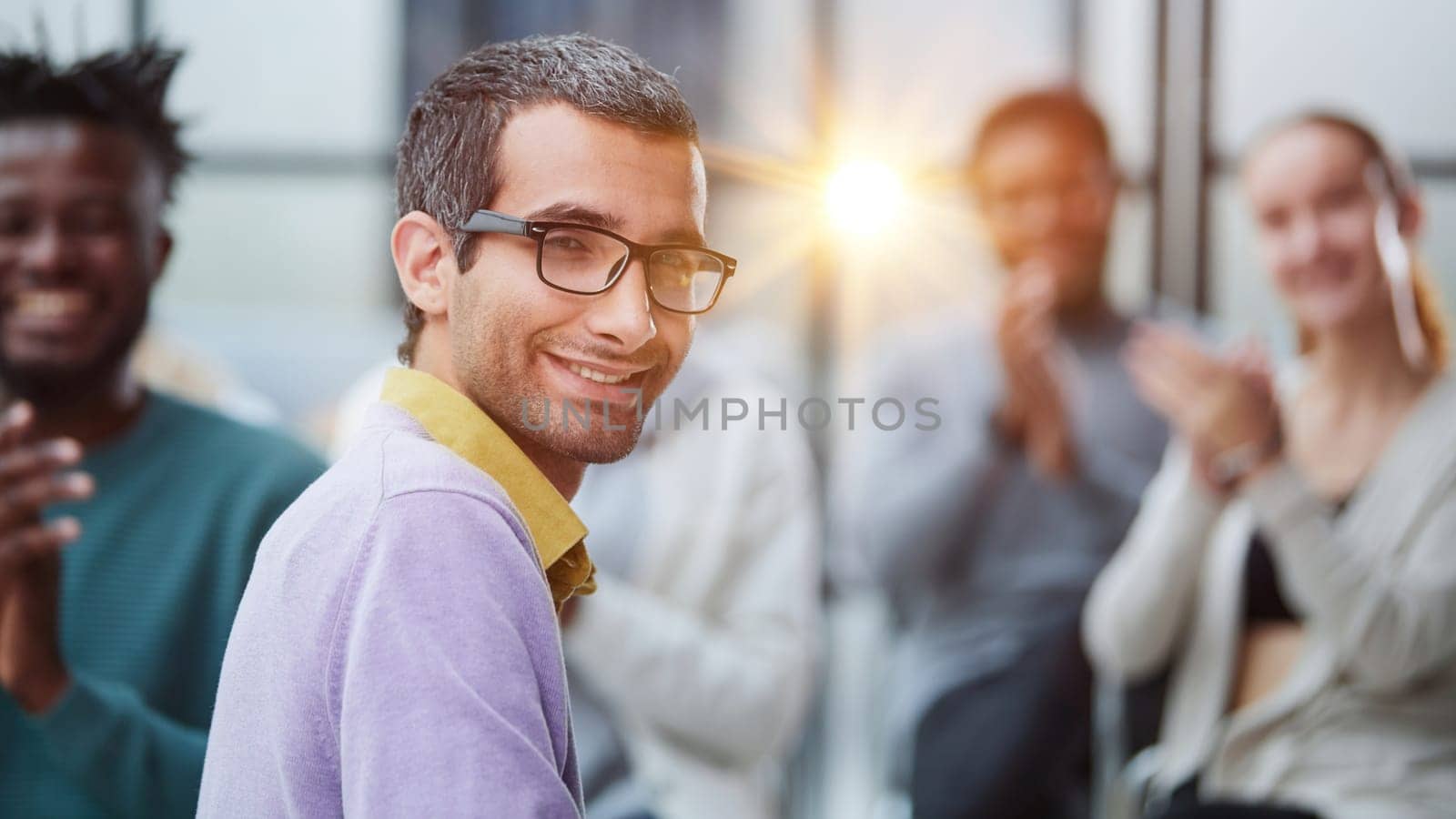 a man in casual clothes with glasses looks at the camera while sitting together with his colleagues by Prosto