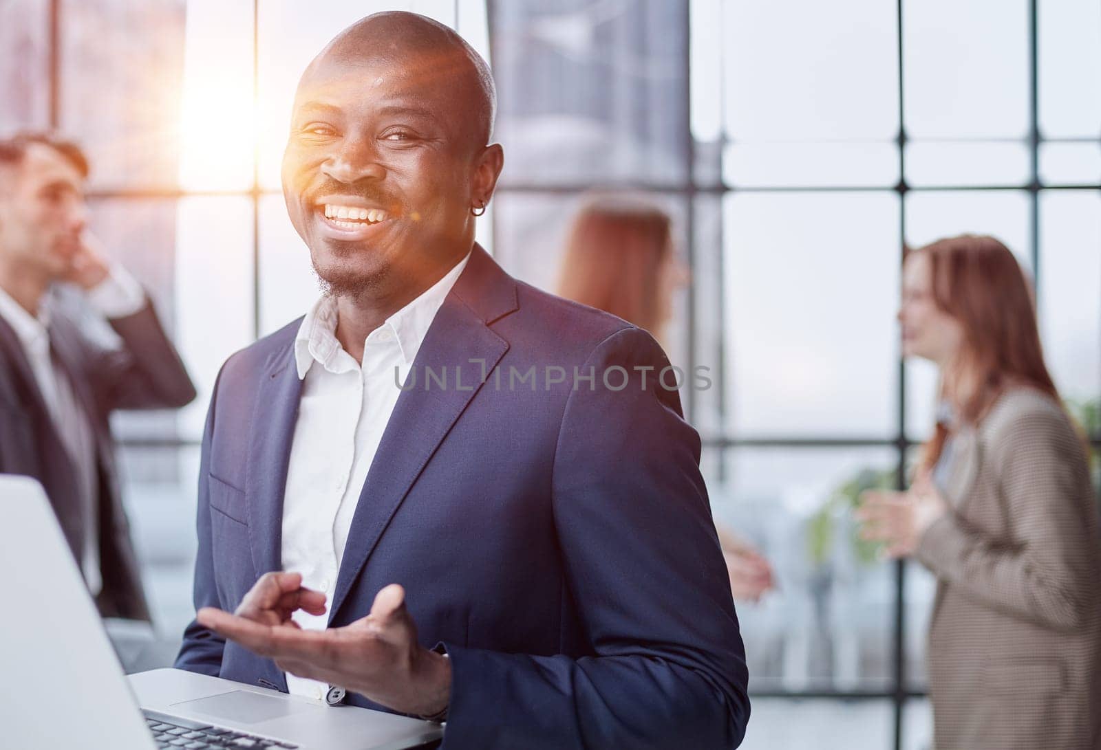 Young african american man in business suit holding laptop while standing at office corridor by Prosto