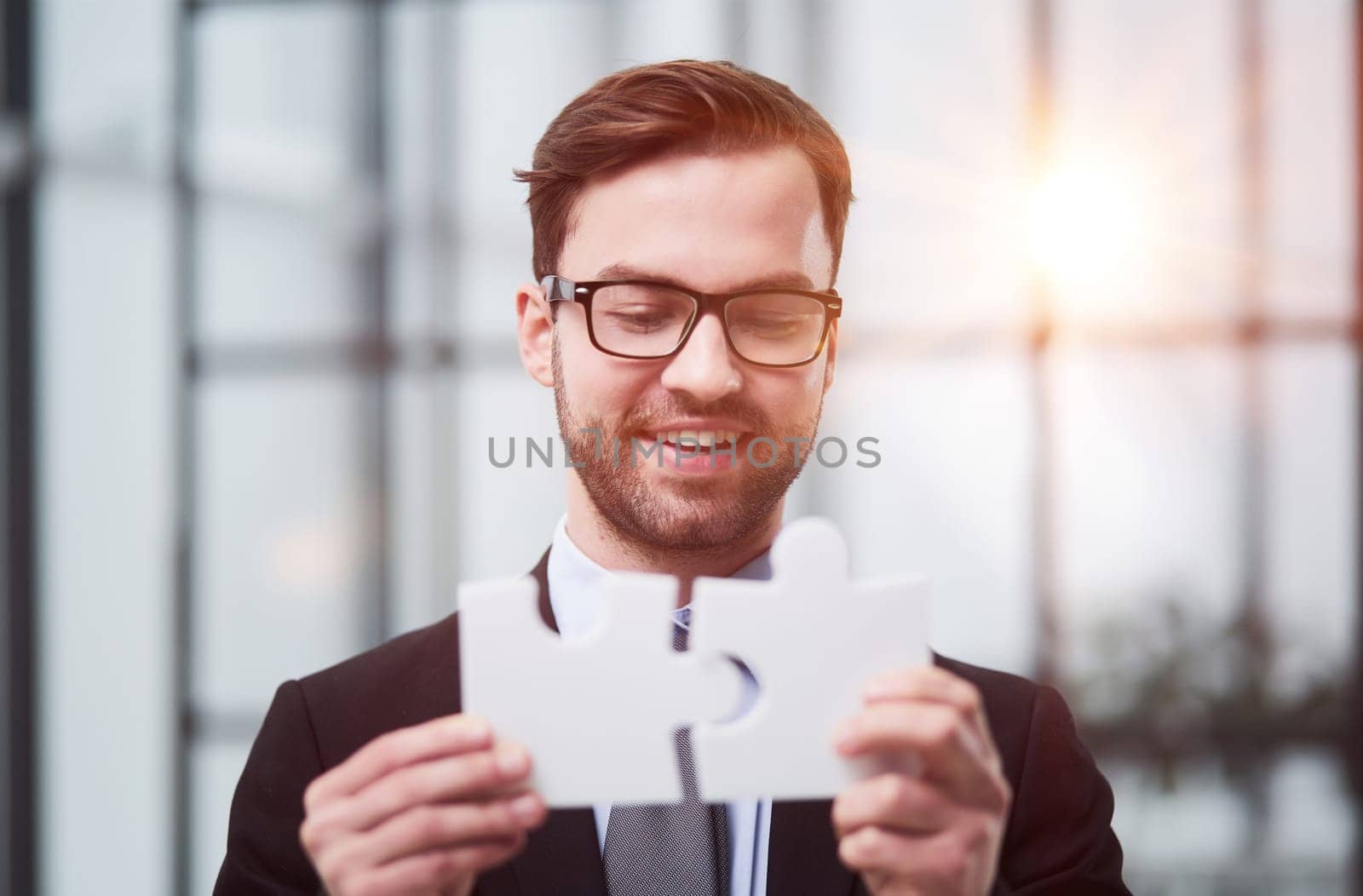 Portrait of an optimistic businessman holding puzzle pieces, solving problems, looking at the camera, wearing a black suit.