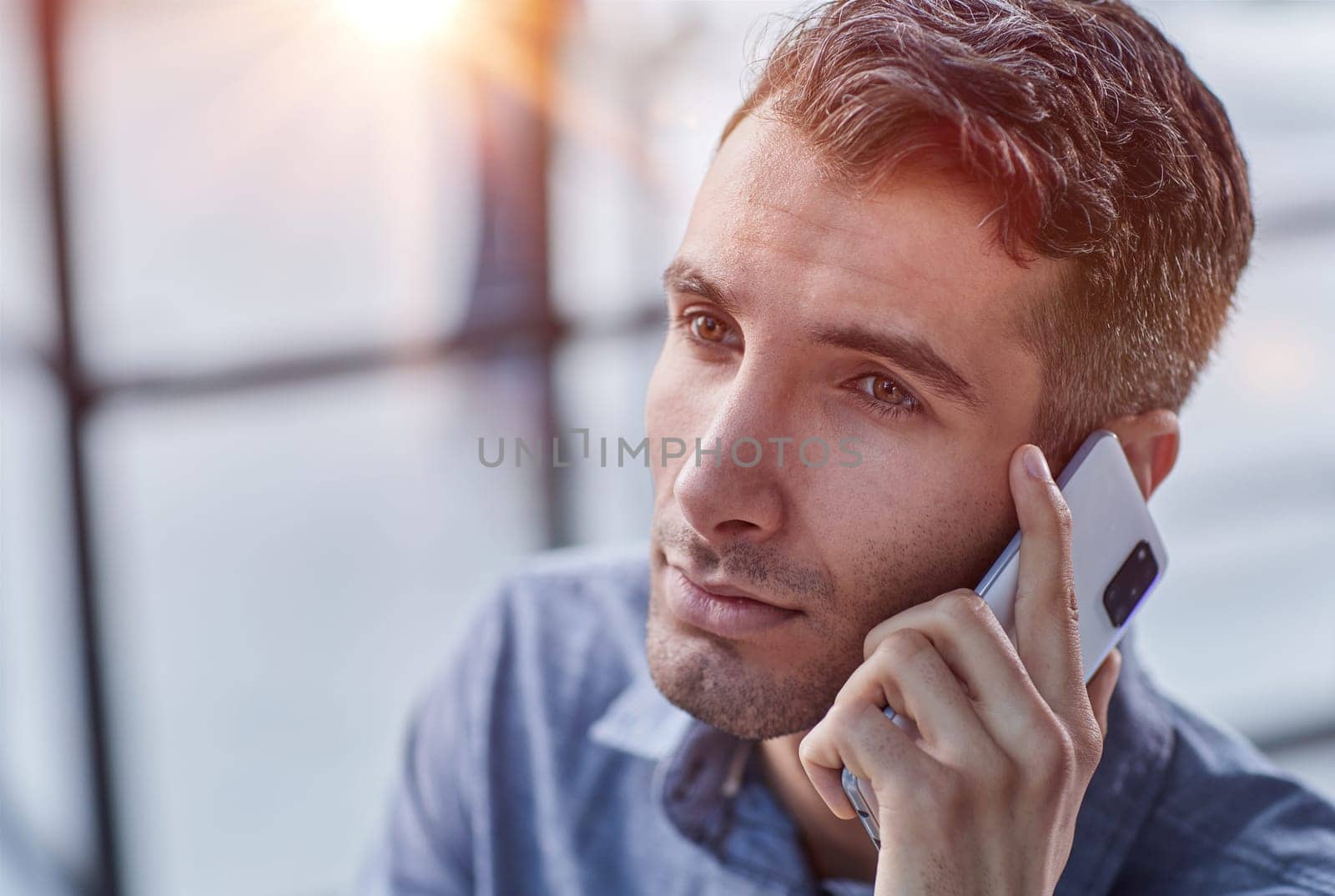Portrait of young entrepreneur in casual office making phone call while working with laptop