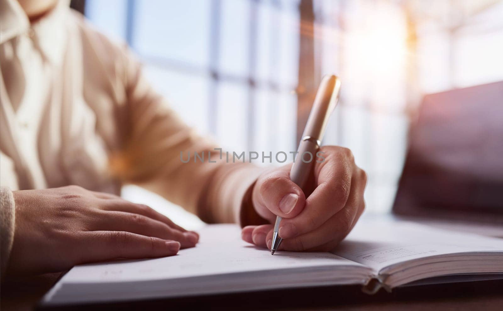 Businessman writes with a pen in diary in a sunny office, business and education concept. Close up