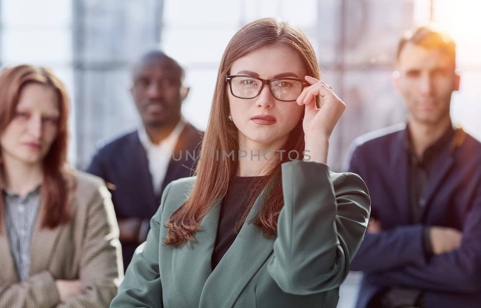 Young executive smiling and standing in a bright room with her team behind her