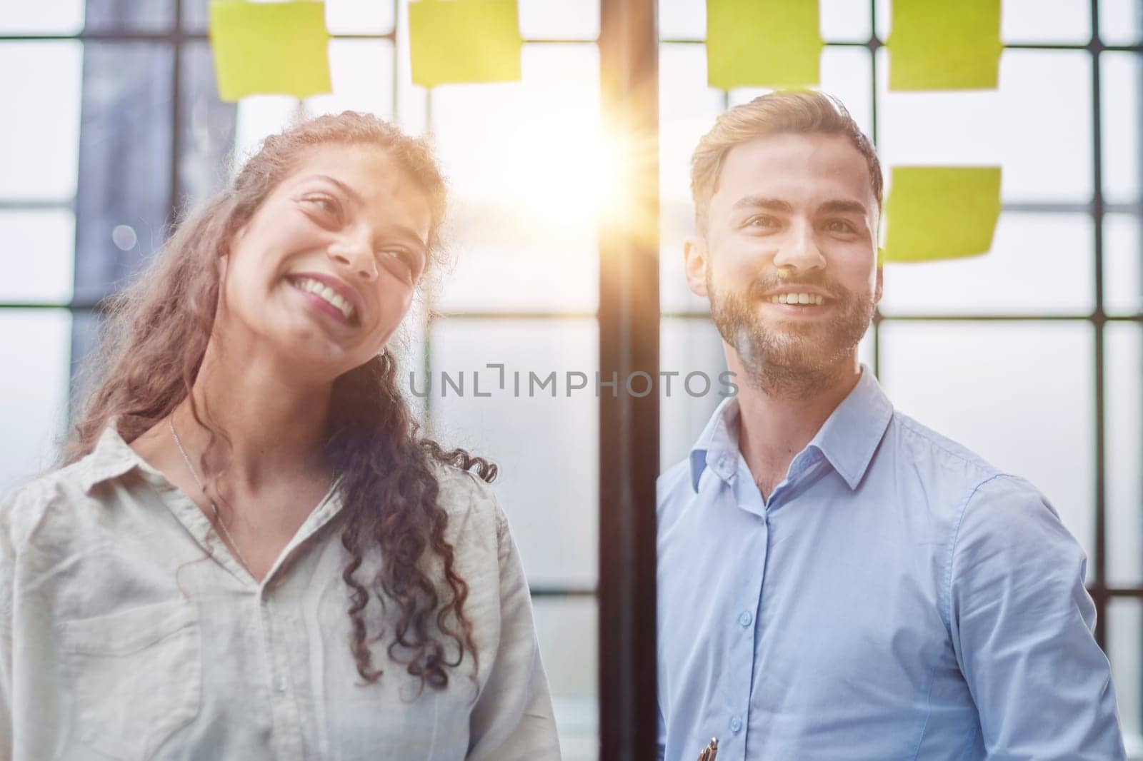 Creative professionals standing and discussing in office behind glass wall with sticky notes