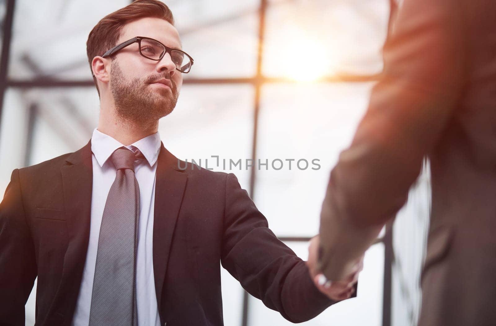 Friendly male professional colleagues greeting handshaking meeting in company office hall