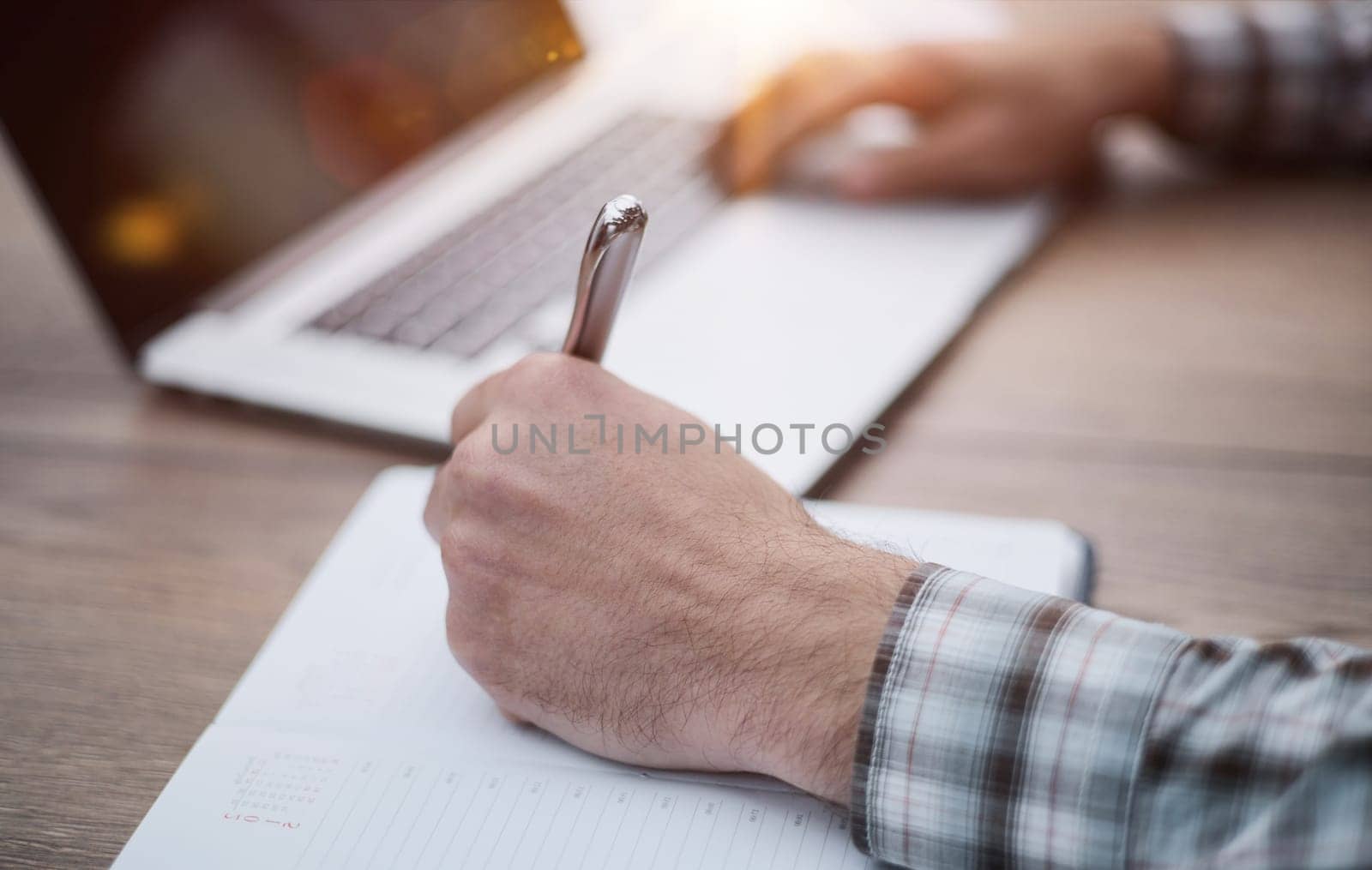Hands writes a pen in a notebook, computer keyboard in background