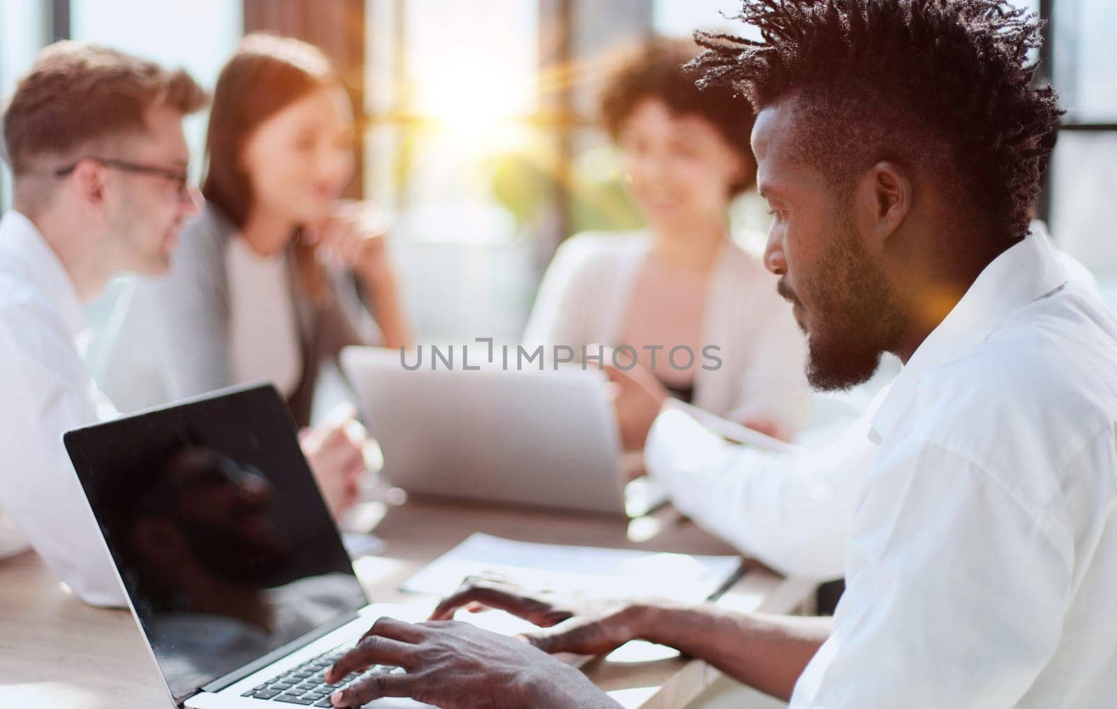 Portrait of smiling African American business man with executives working on laptop in background.