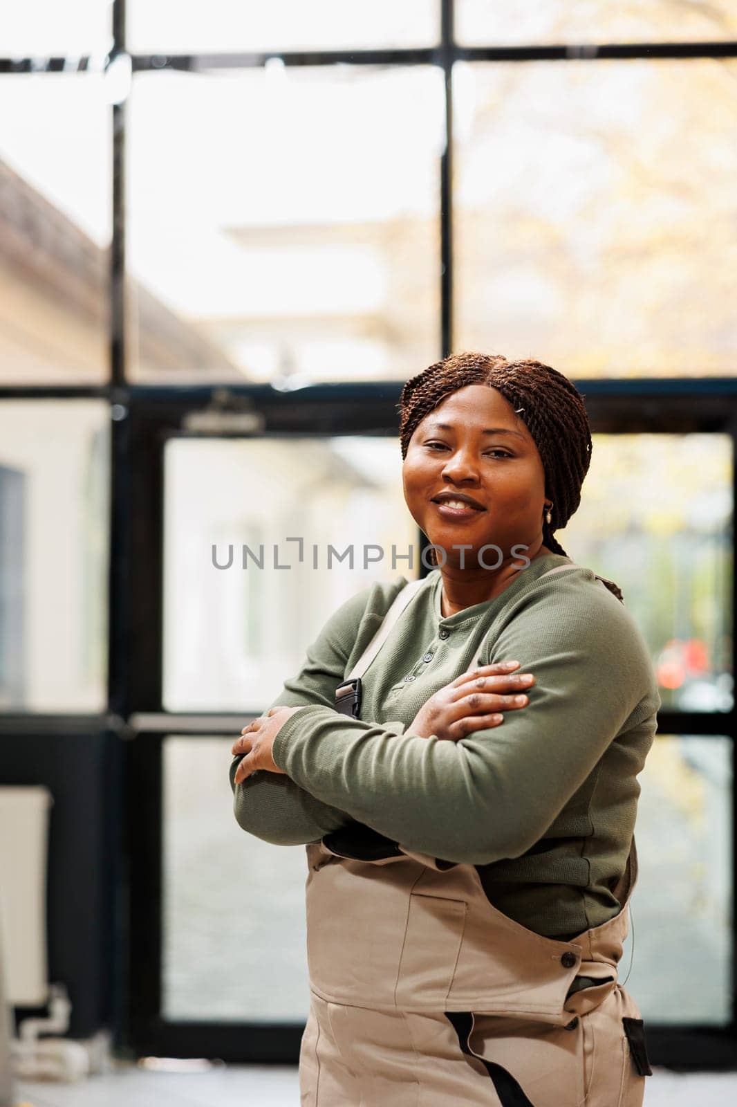 Smiling storage room worker standing with arm crossed, posing with confidence in front of camera. African american manager wearing industrial overall while working at customers online orders