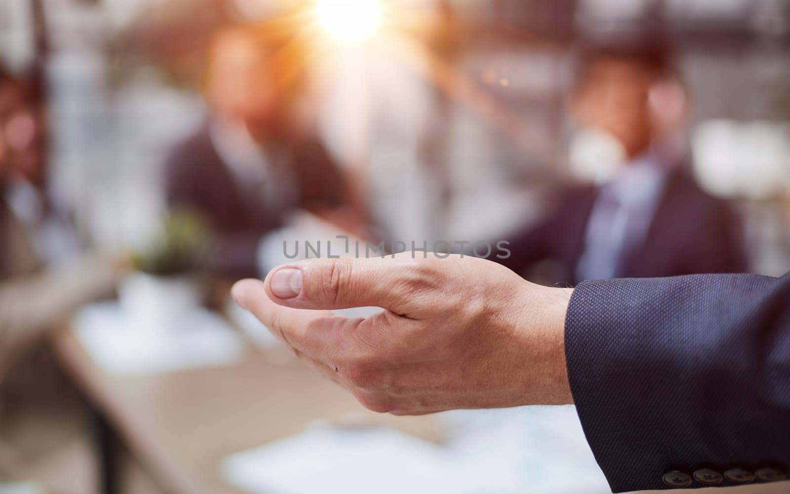 The hand of a man in a suit stretches to the side against the background of blurred colleagues. by Prosto