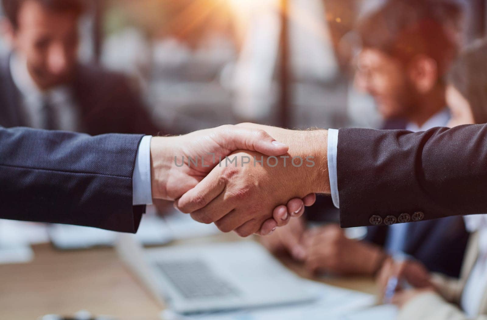 Close up view of two unrecognizable people shaking hands in office against work meeting background