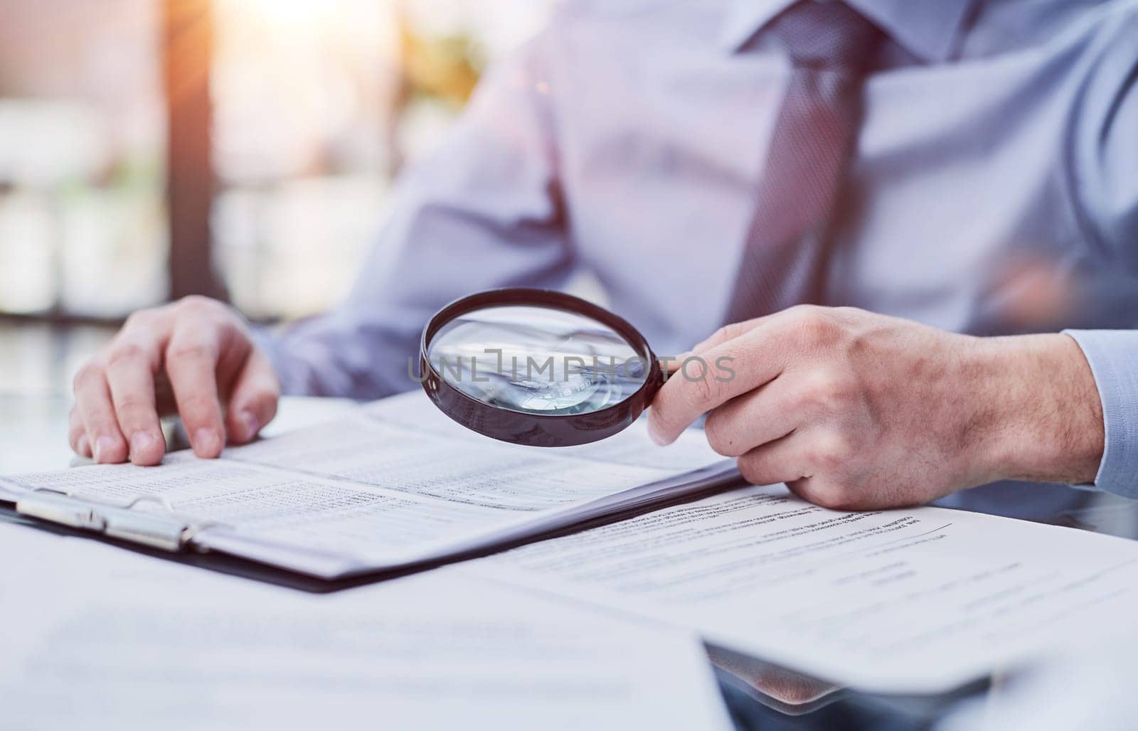 Businessman looking through a magnifying glass to documents by Prosto